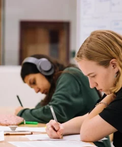 Dva učenca sedita za mizo in pišeta zapiske